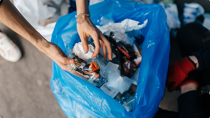 Hände die Plastikmüll in einen blaue Tüte einfüllen